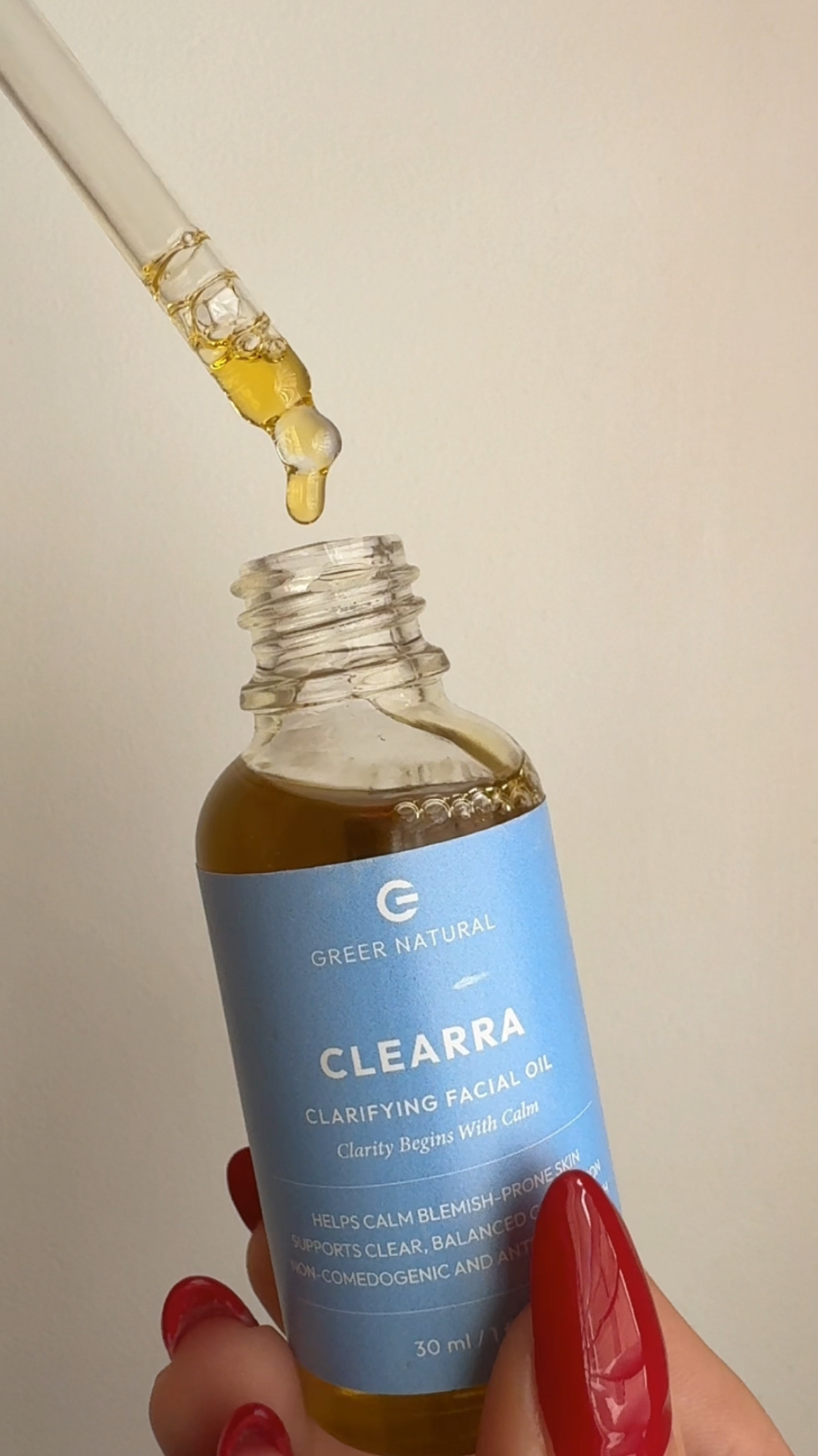 Clearra facial oil with dropper held by a hand against a neutral background