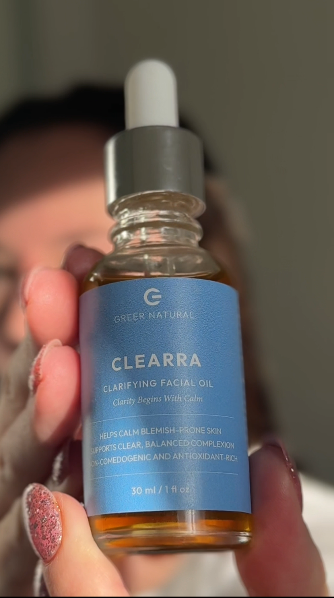 Clearra clarifying facial oil bottle held by a person with pink nail polish.