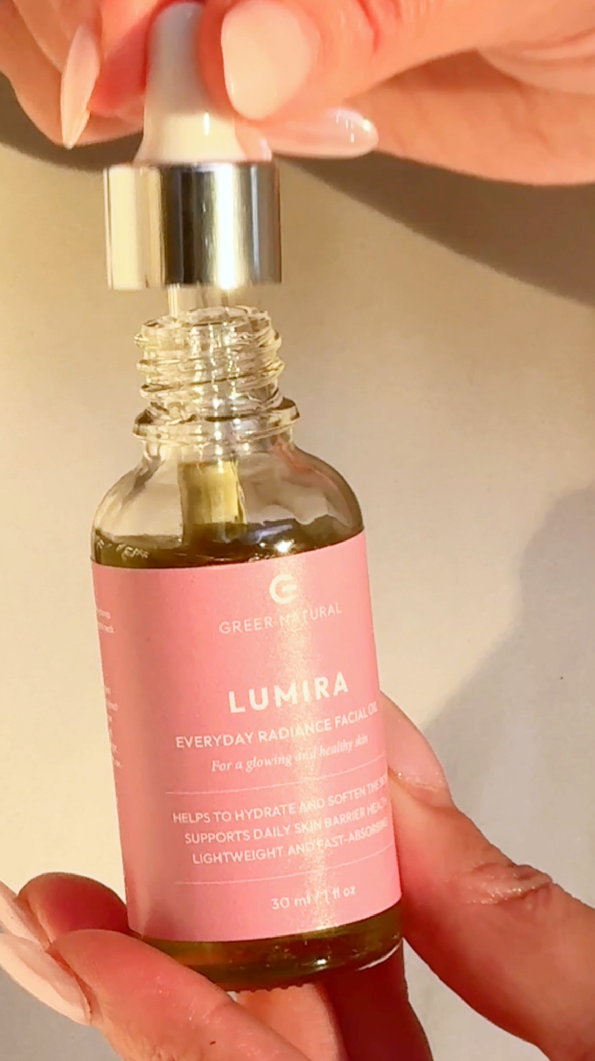 Bottle of Greer Natural Lumira facial oil held by a hand with pink nail polish.