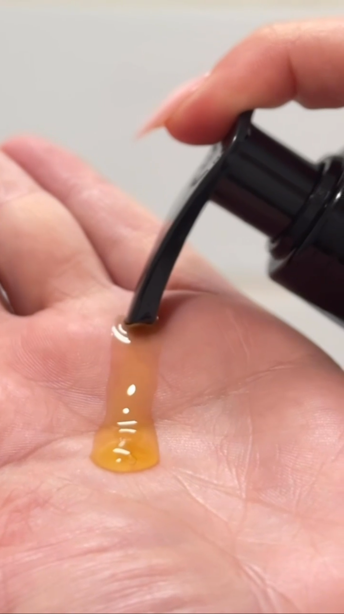 Hand holding a small bottle with a dropper filled with Novaglow body oil against a neutral background